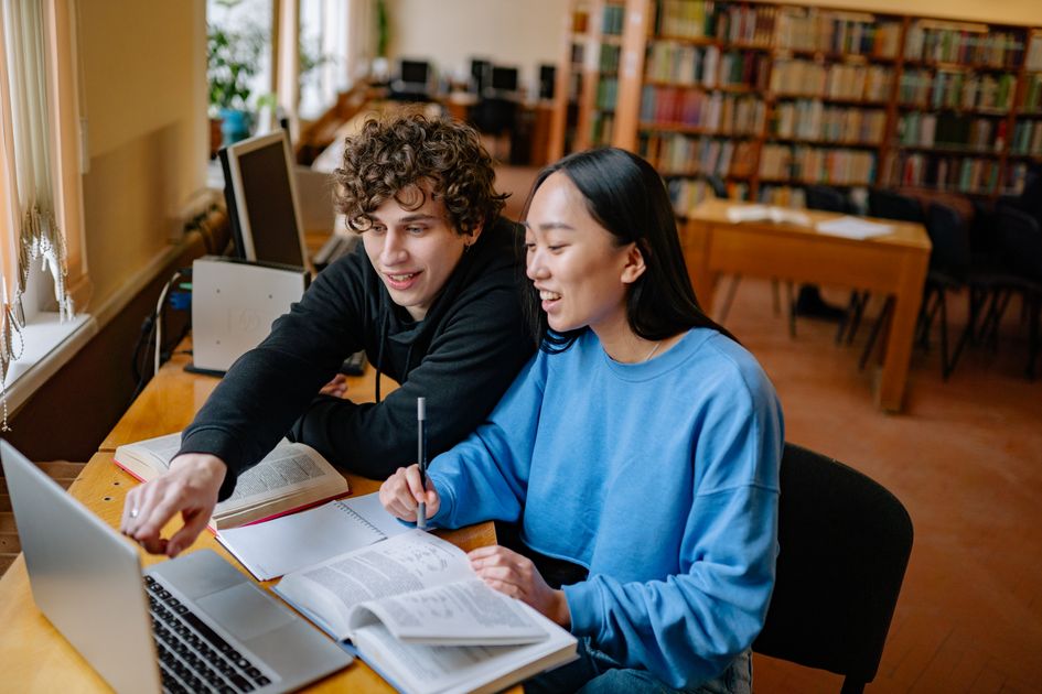 Students studying together in a library with a laptop and open books.